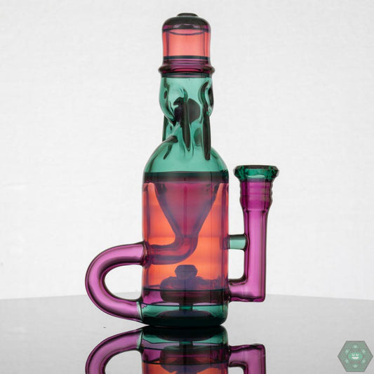  Jack Blew – Mini Ramune Bottle Recycler with 4-Hole Perc. Precision Design: Crafted by Jack Blew Glass, showcasing expert glasswork. Efficient Filtration: Equipped with a 4-hole perc, 10mm female 90° joint, and single drain for smooth recycling. Compact & Stylish: Compact 6" height and 2.5" diameter with a fully faceted joint for added sophistication. Premium Additions: Includes a Headdy Mood Mat, sticker, and business card for added value. Collector's Item: Combines functionality with artistic aesthetics.