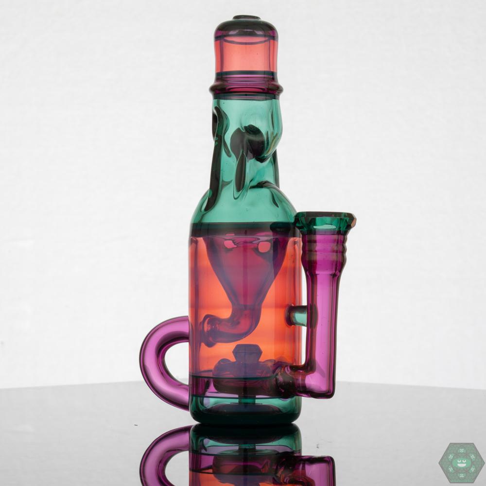 Jack Blew – Mini Ramune Bottle Recycler with 4-Hole Perc. Precision Design: Crafted by Jack Blew Glass, showcasing expert glasswork. Efficient Filtration: Equipped with a 4-hole perc, 10mm female 90° joint, and single drain for smooth recycling. Compact & Stylish: Compact 6" height and 2.5" diameter with a fully faceted joint for added sophistication. Premium Additions: Includes a Headdy Mood Mat, sticker, and business card for added value. Collector's Item: Combines functionality with artistic aesthetics.